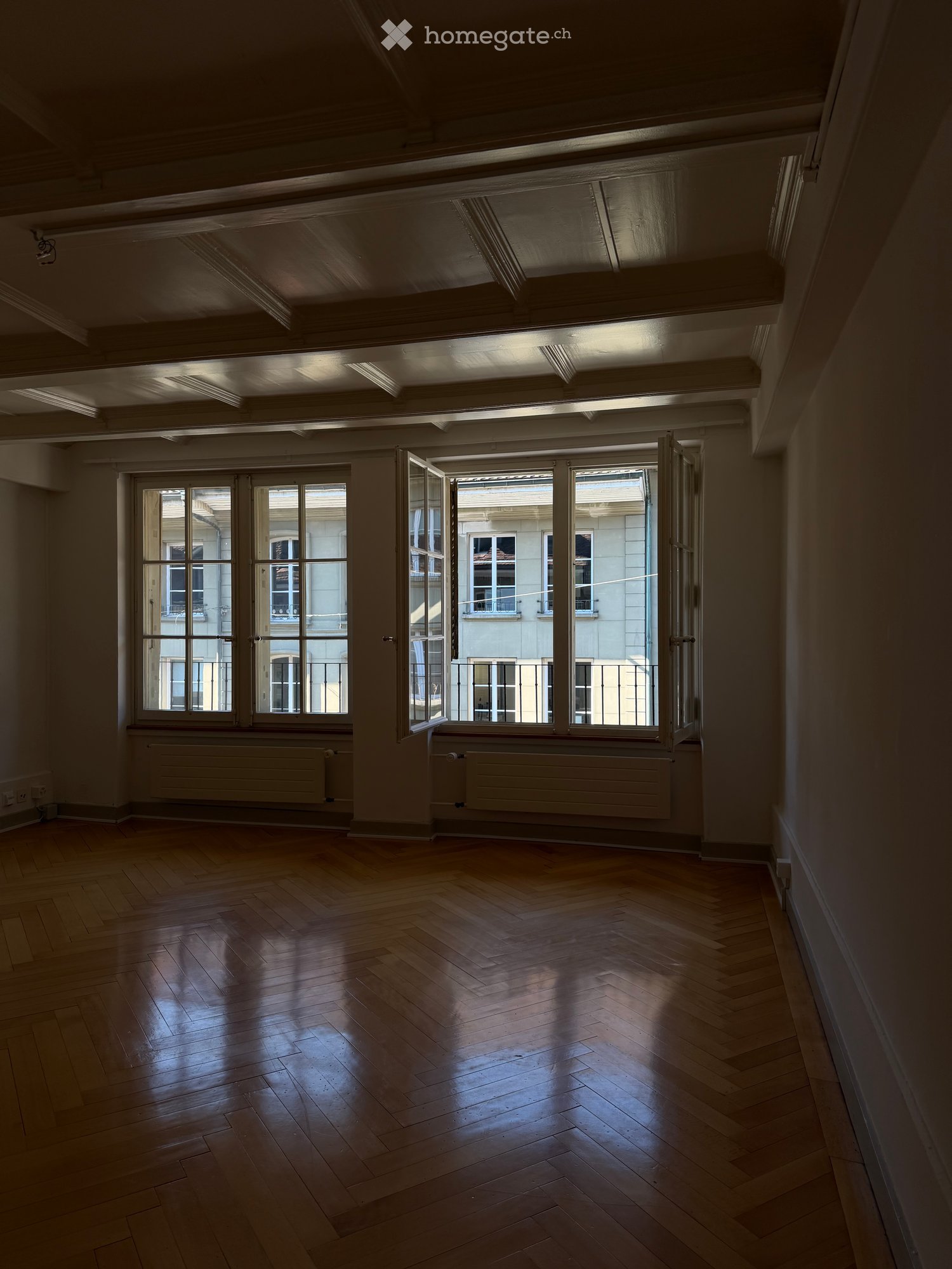 Empty room with wooden flooring, large windows, and radiators. No furniture or equipment present.