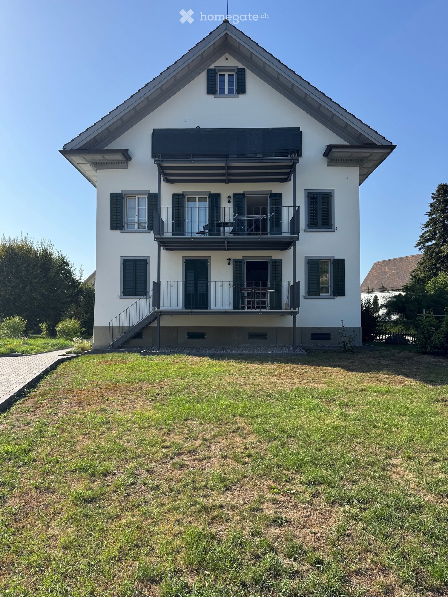 Two-story white house with black shutters, multiple balconies, and a well-maintained lawn.