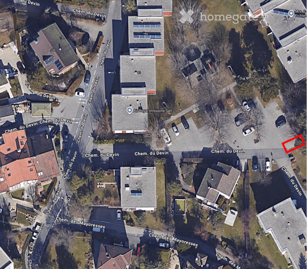 Aerial view of a residential area showing multiple buildings, streets, and parked cars. The highlighted building is a two-story structure with a flat roof and multiple windows.