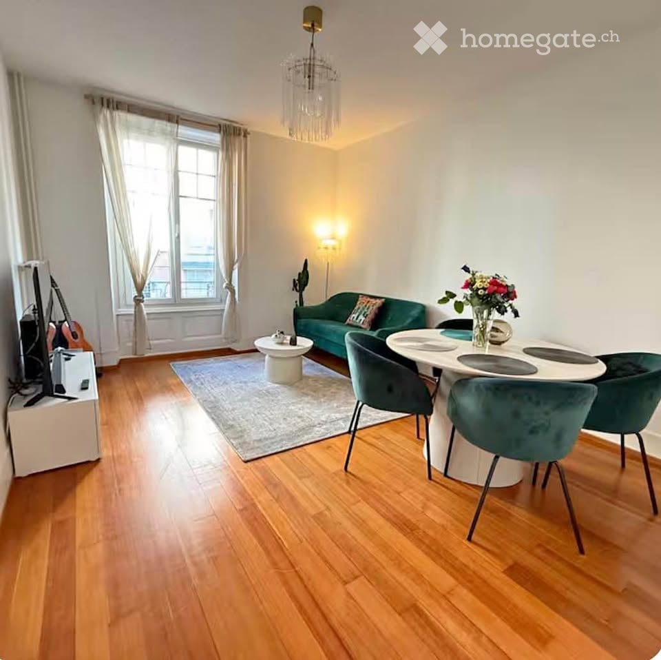 A modern living and dining area with wooden flooring, a green sofa, a white dining table with green chairs, a chandelier, and a guitar in the corner.