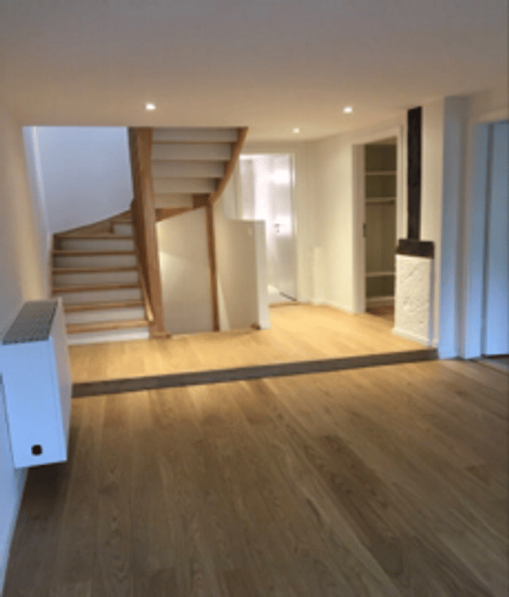 Empty room with wooden flooring, a staircase leading upwards, and recessed lighting. No furniture or equipment is present.