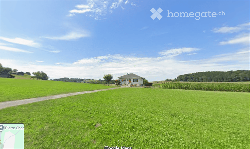 A single-story house with a red and white exterior, situated in a lush green field with a clear blue sky and scattered clouds in the background.