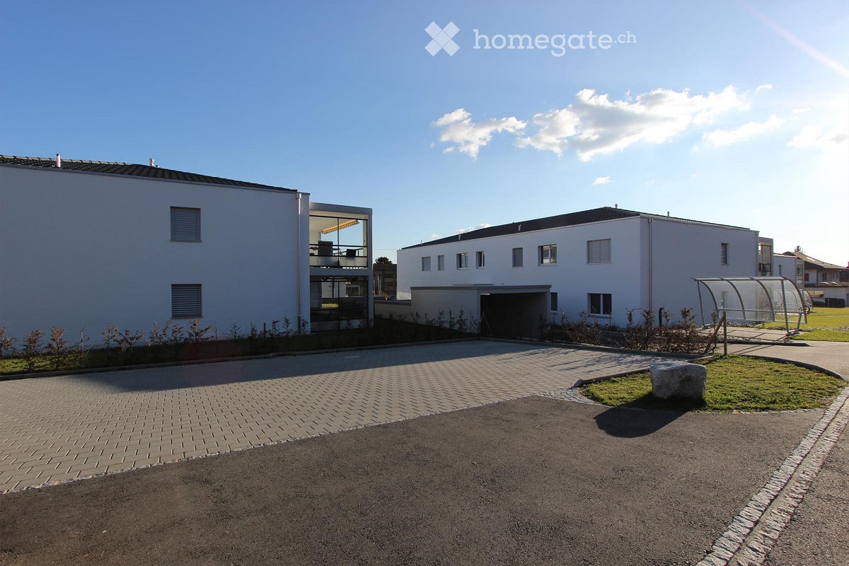 Modern two-story building with white exterior, garage, and small landscaped area with a stone and grass patch.