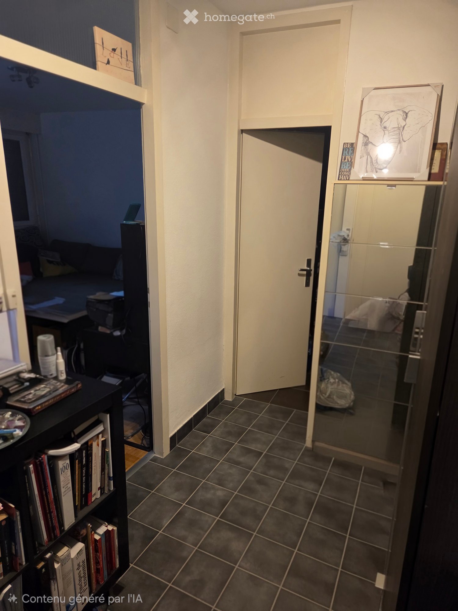A narrow hallway with dark tiled flooring, white walls, and a closed door leading to another room. A bookshelf with books and a small table with items are visible on the left side.