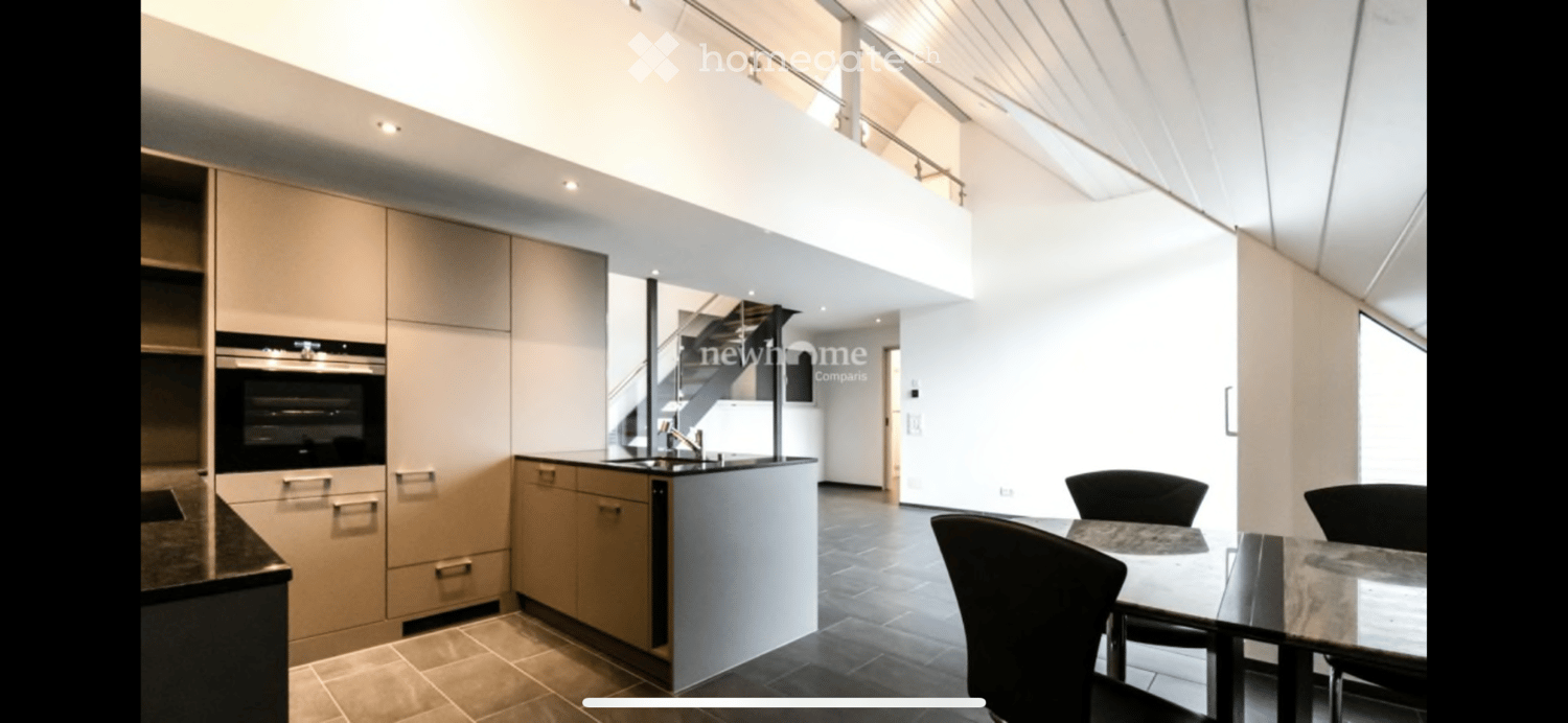 Modern kitchen with light-colored cabinets, built-in oven, and a small dining area with a table and chairs. The space features a sleek, contemporary design with a raised platform leading to an upper level.