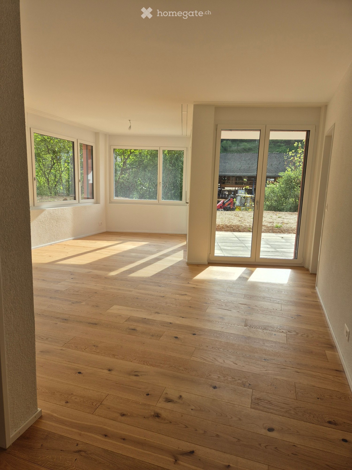 Empty room with wooden flooring, large windows, and sliding glass doors leading to an outdoor area.