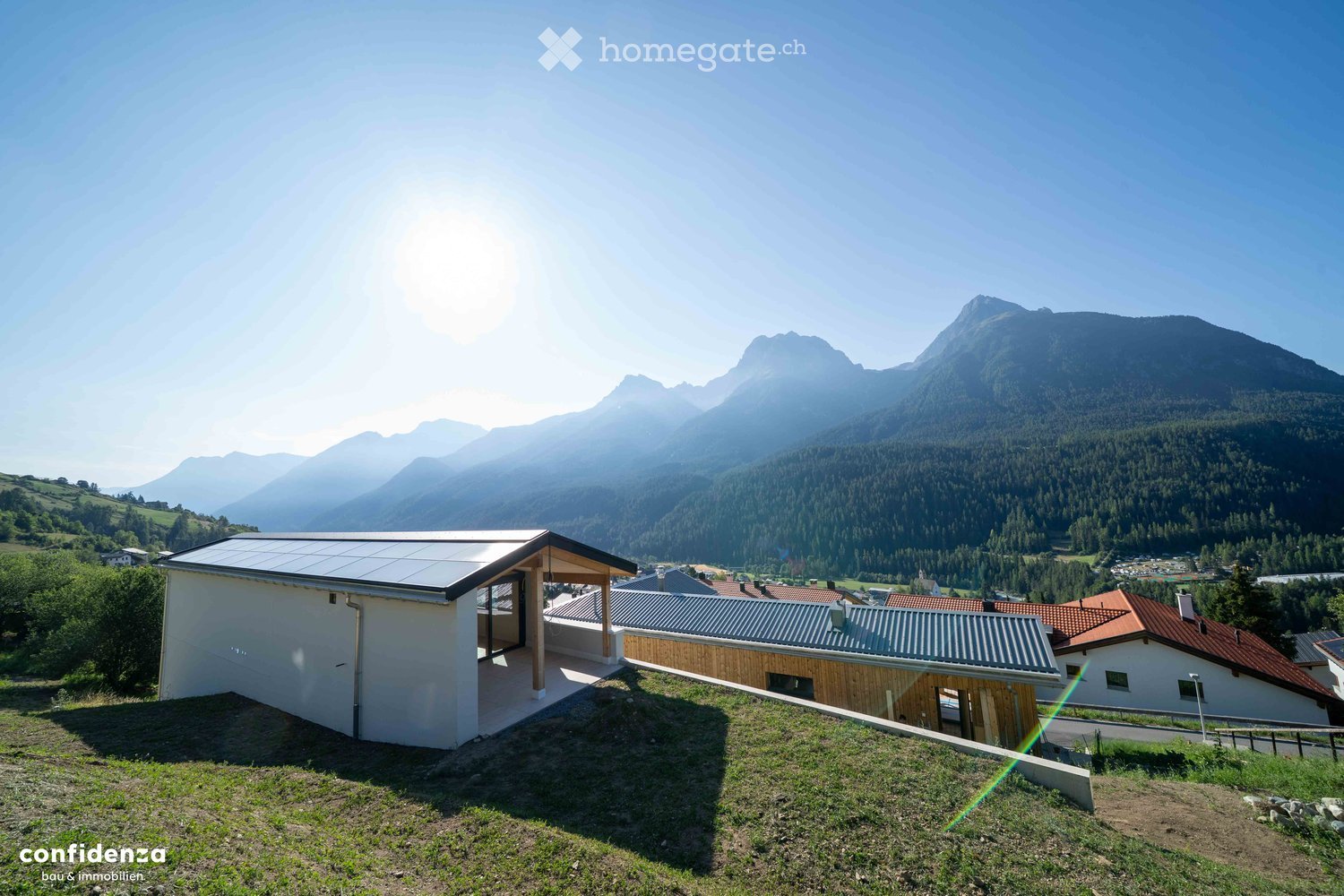 Modern house with solar panels on the roof, surrounded by a lush green landscape and distant mountains.