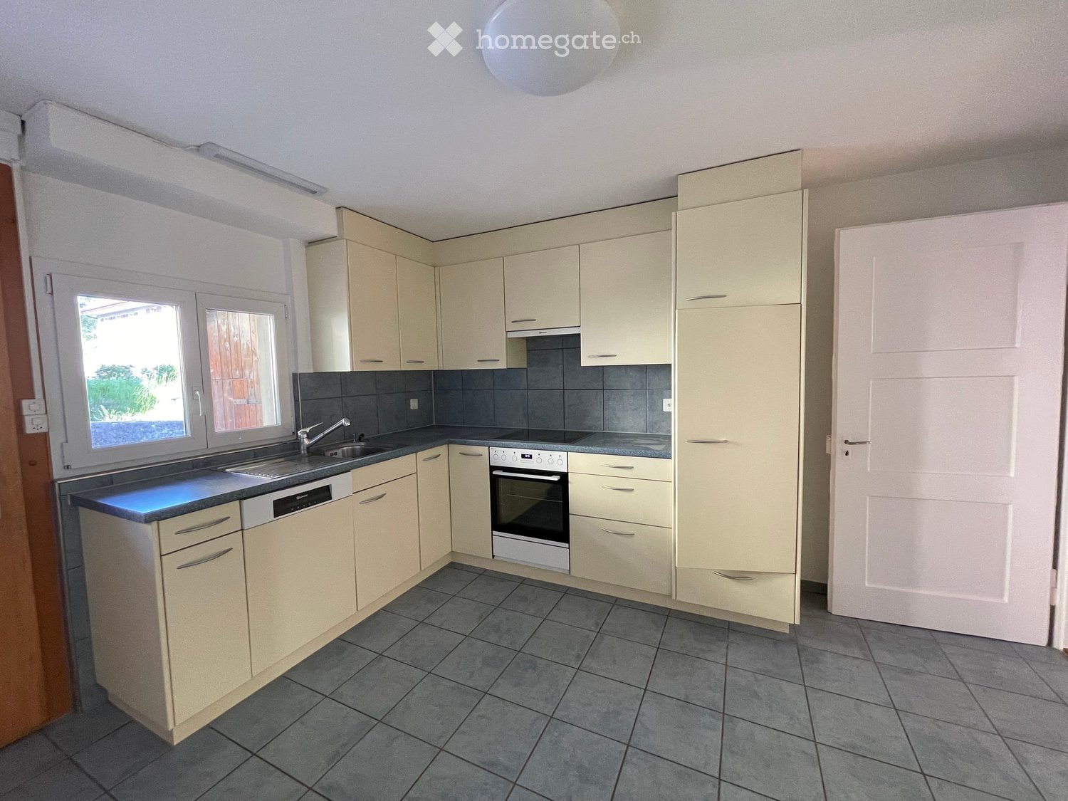 Modern kitchen with light-colored cabinets, stainless steel appliances, and a tiled floor.