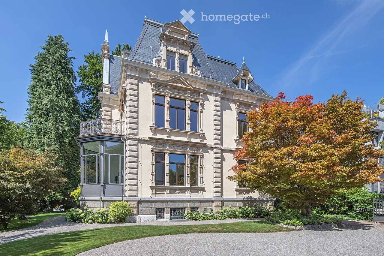 Large, elegant mansion with multiple stories, ornate architectural details, large windows, and a well-maintained garden.