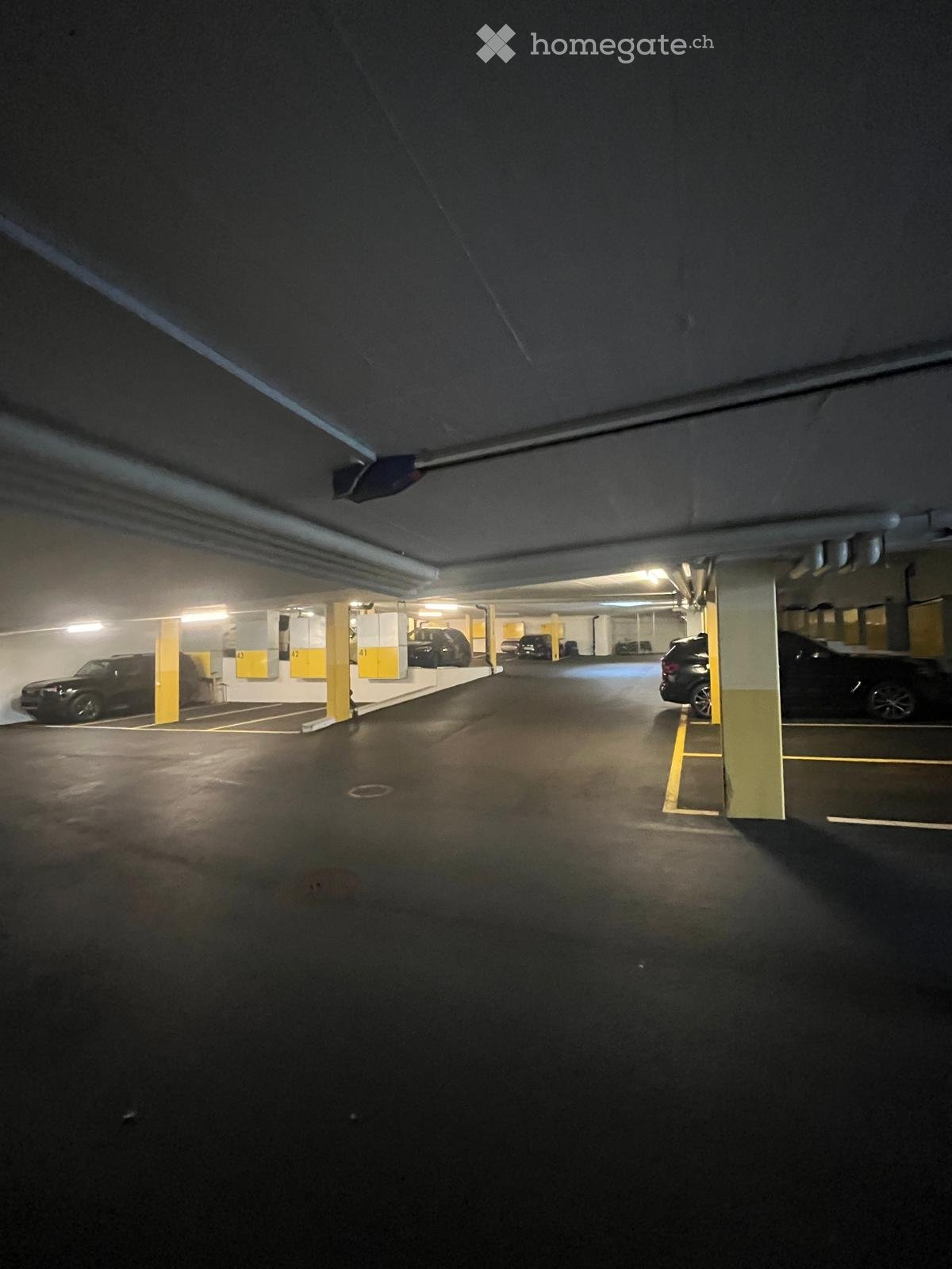 Underground parking area with several parked cars, marked parking spaces, and yellow painted pillars.