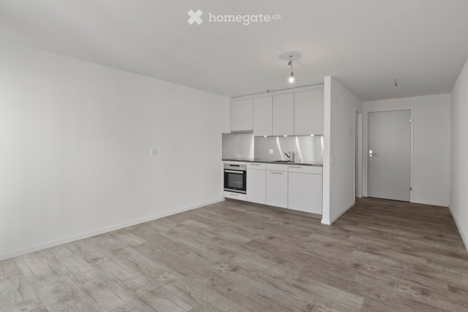 Empty kitchen with white cabinets, stainless steel appliances, and wooden flooring.