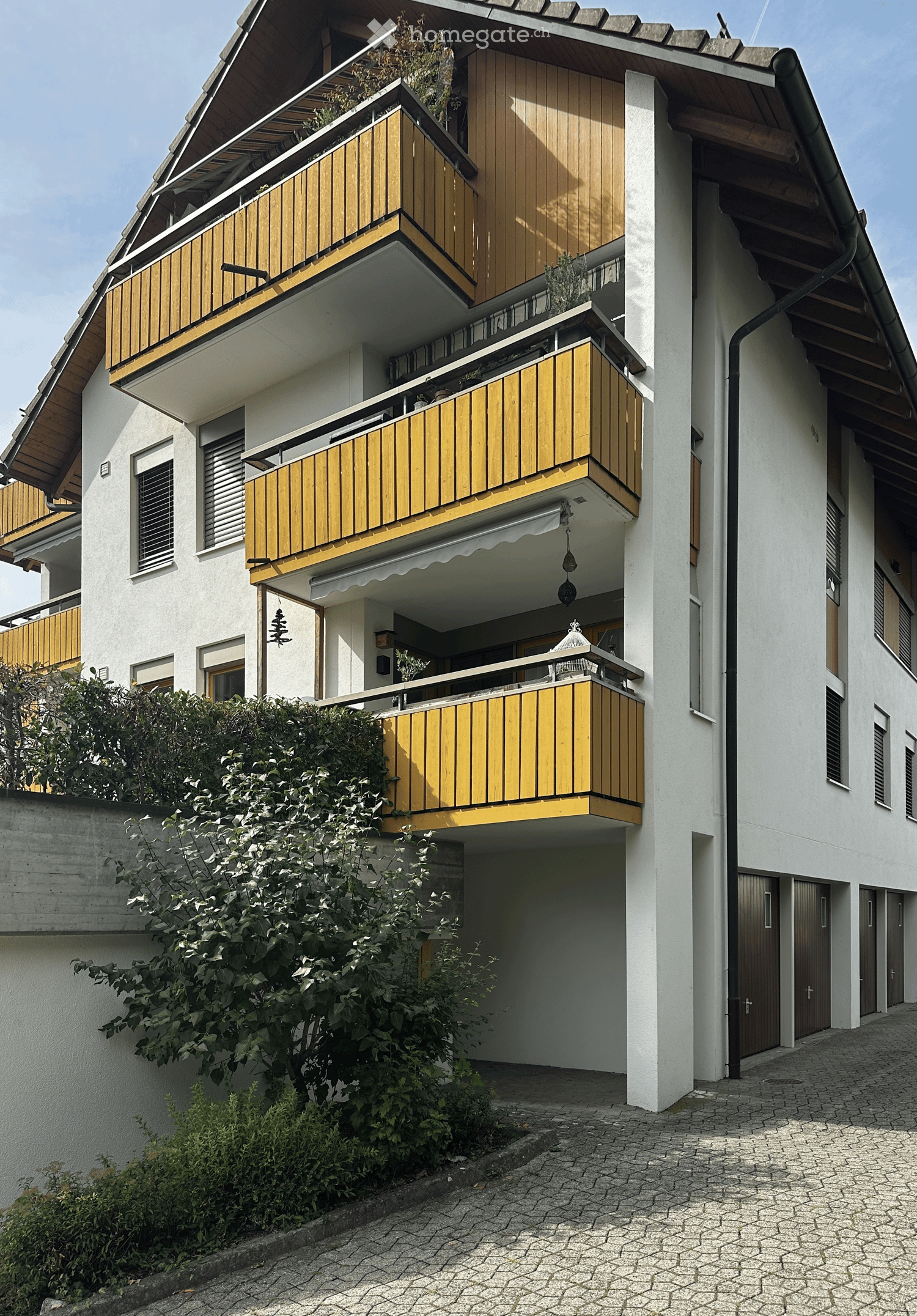Multi-story residential building with white walls, wooden balconies, and multiple windows.