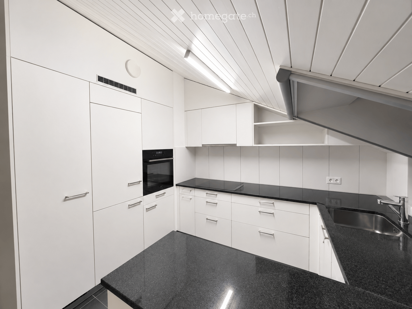 Modern kitchen with white cabinets, black countertops, stainless steel sink, and built-in oven.