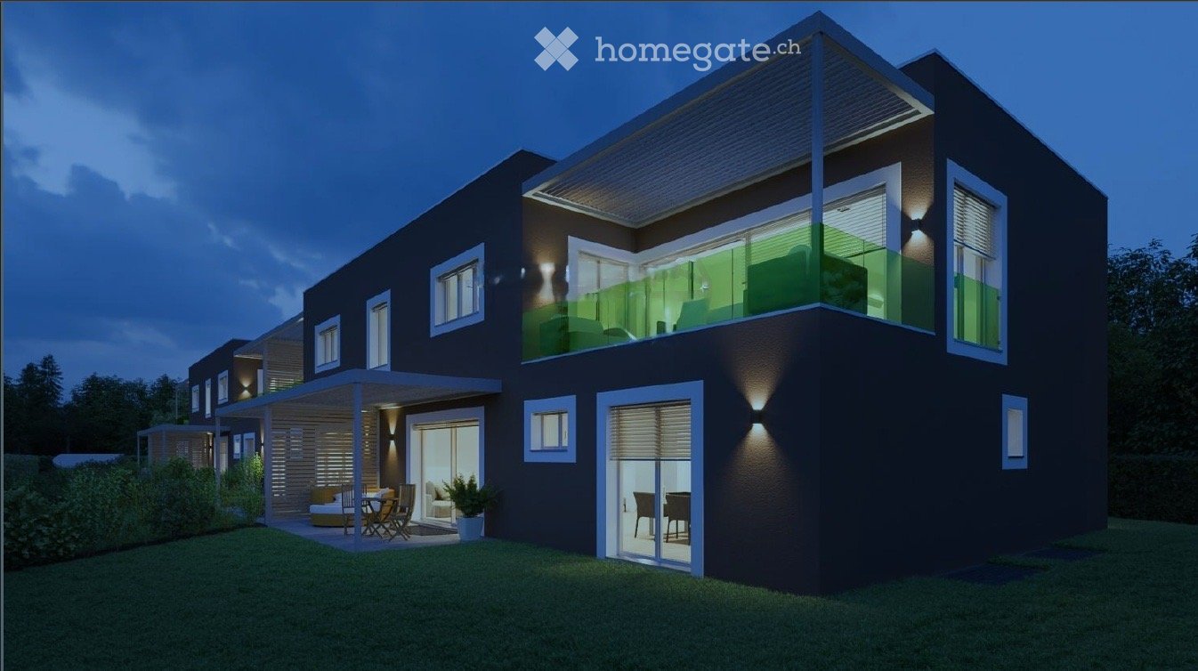 Modern two-story house with dark exterior, large windows, and a balcony on the upper level. The ground floor features a covered patio area with outdoor furniture.
