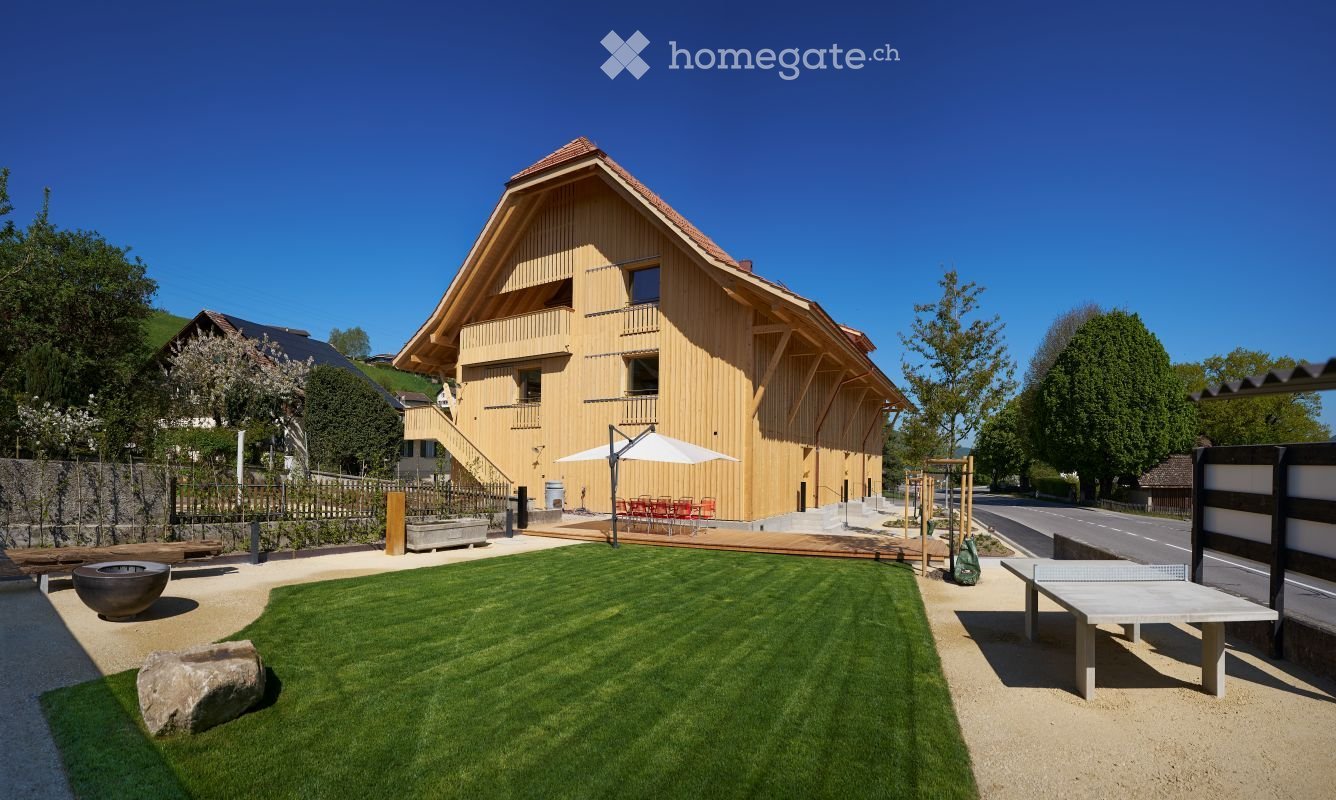 A modern wooden house with a spacious garden, featuring a lawn, patio, outdoor seating, and a ping pong table.