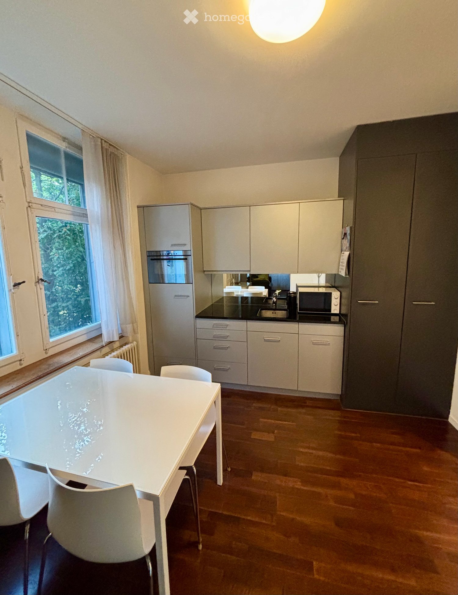 Modern kitchen and dining area with white cabinets, a black countertop, a white dining table with four chairs, and a microwave on the counter.