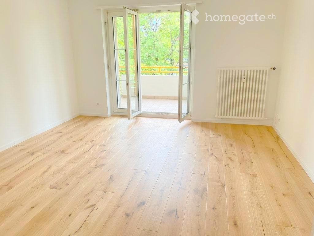 Empty room with light wooden flooring, white walls, and a large open sliding door leading to a balcony.