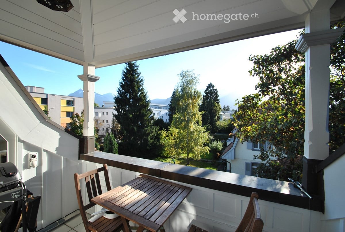 Balcony with wooden table and chairs, overlooking a scenic view of trees and mountains.