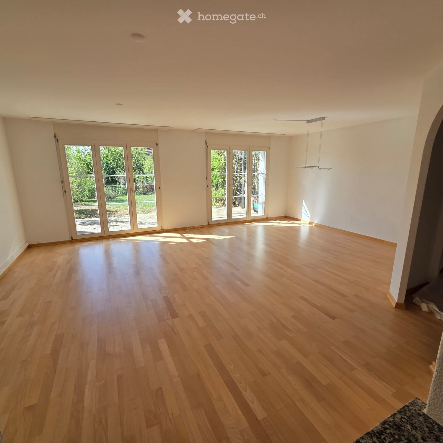 Empty room with light wooden flooring, white walls, and large glass doors leading to an outdoor area.