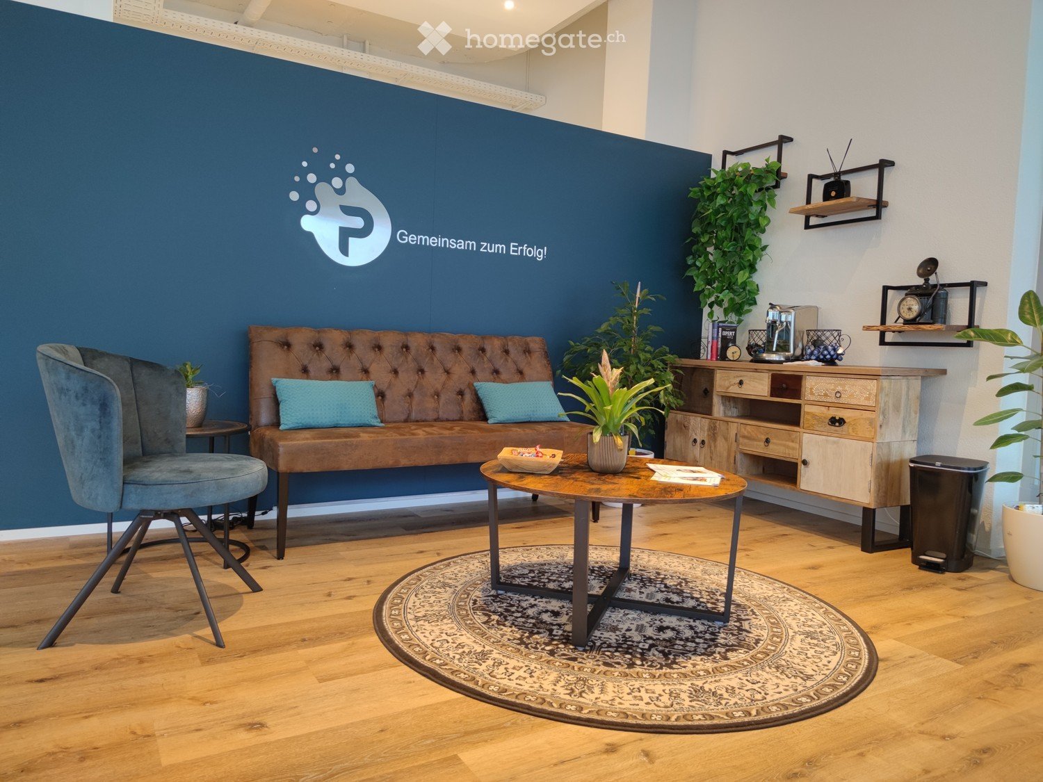 Blue wall, round rug, round table, wooden couch with pillows, blue chair, desk with drawers