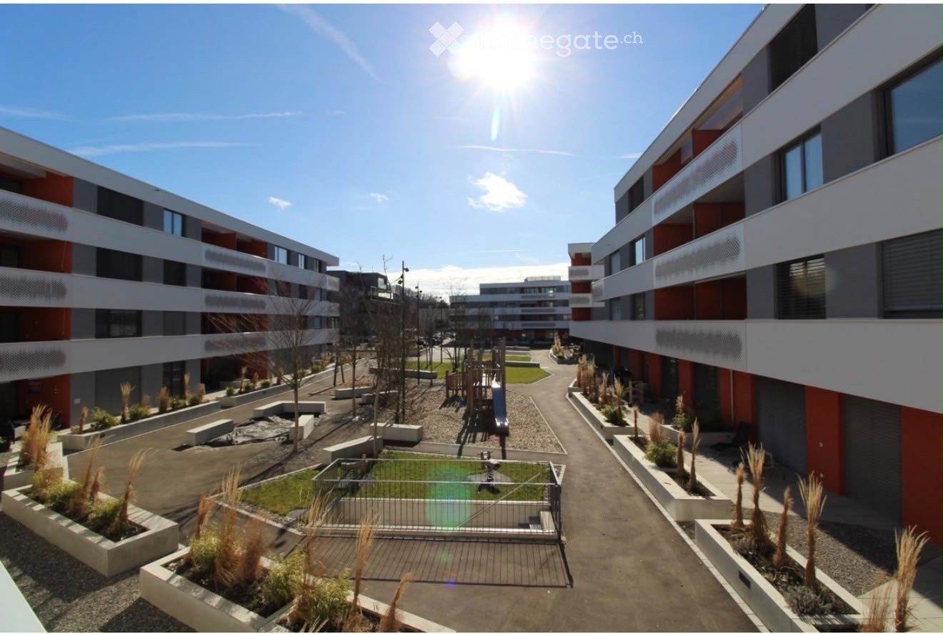 Courtyard view of a modern residential complex with multi-story buildings, landscaped areas, playground, and small garden beds.