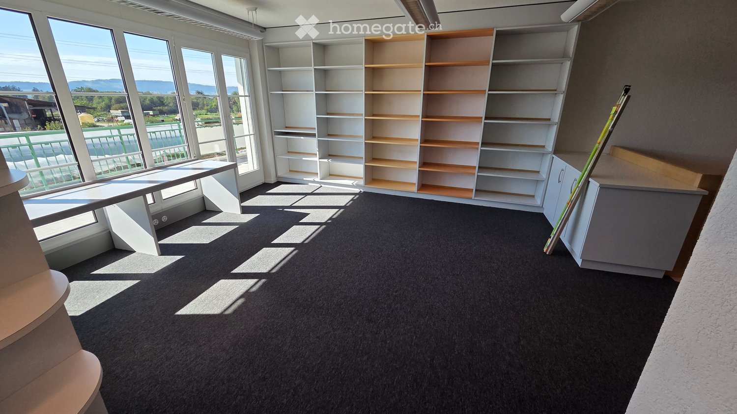 Empty room with large windows offering a scenic view, featuring built-in shelving units and a small table.