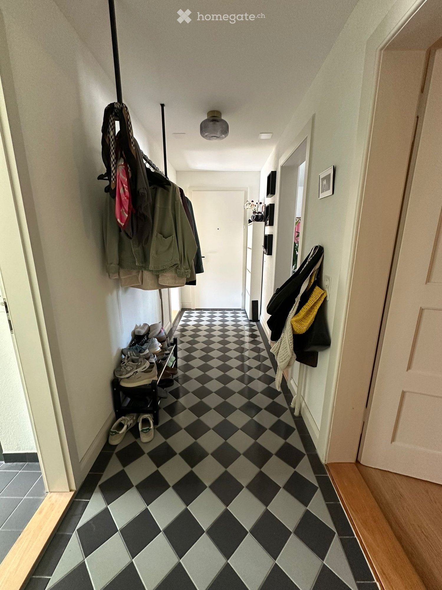 black and white checkered floor, white walls, clothes hanging on the wall, shoes on the rack, picture frame on the wall