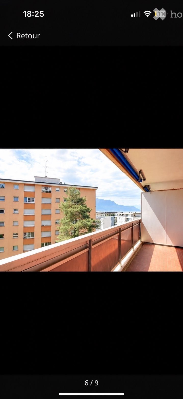 Balcony with wooden flooring, metal railing, and a view of a tree, building, and mountains.
