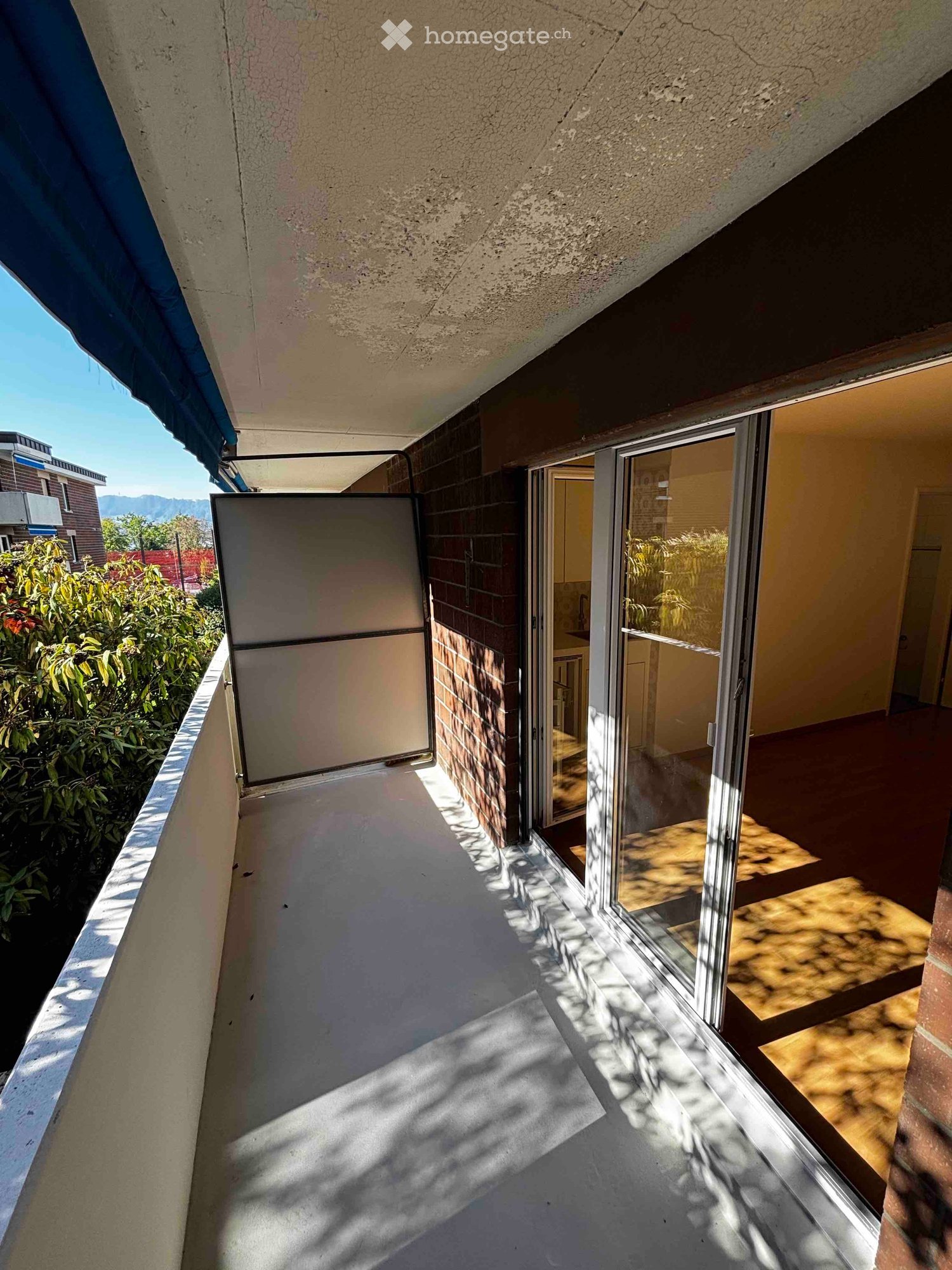 Balcony with a view of greenery, featuring a sliding glass door leading to an interior space.