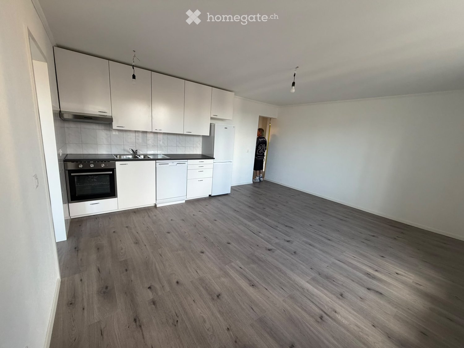 Empty kitchen with white cabinets, stainless steel appliances, and wooden flooring.