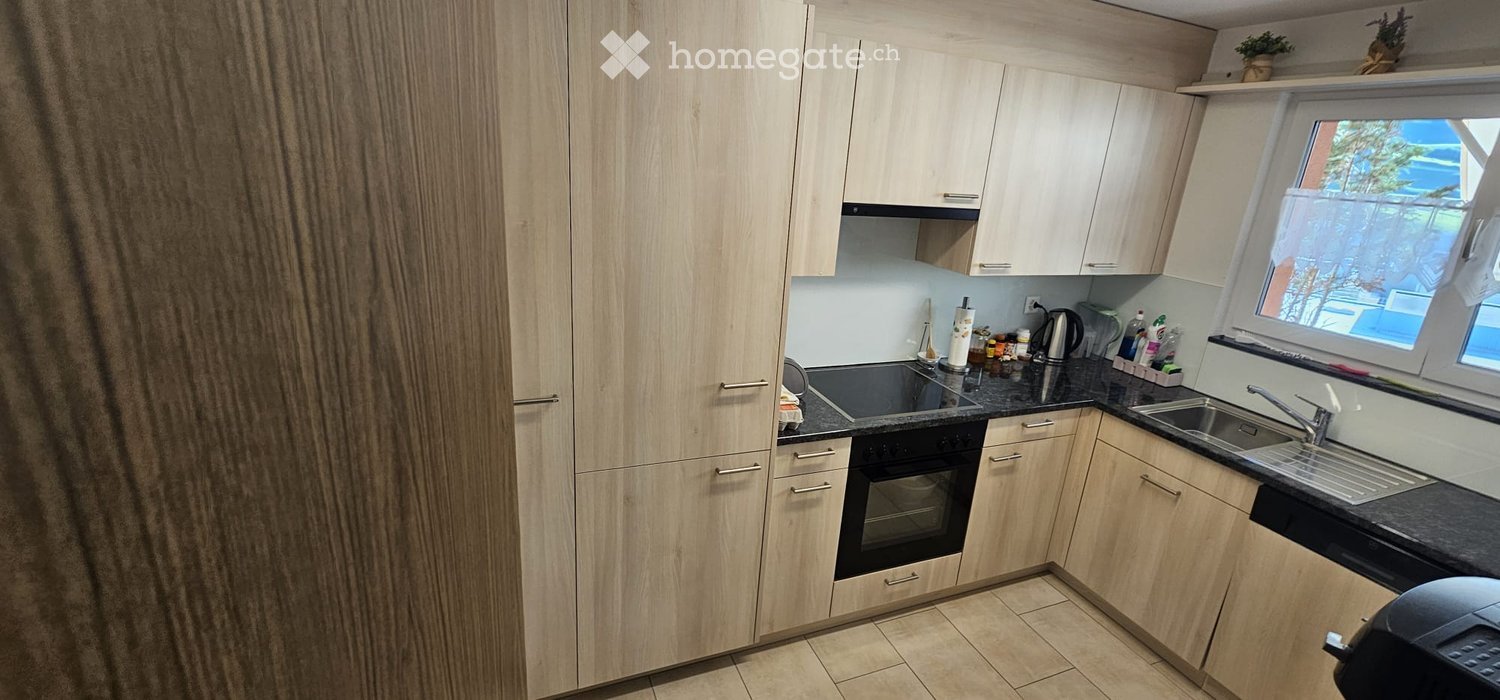 Modern kitchen with light wooden cabinets, black countertop, sink, oven, and various kitchen utensils on the counter.