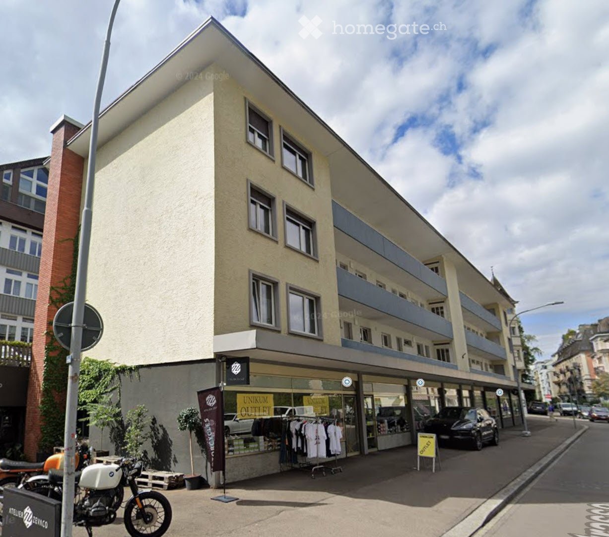 A multi-story building with a modern facade, featuring a storefront with clothing racks and a motorcycle parked outside.