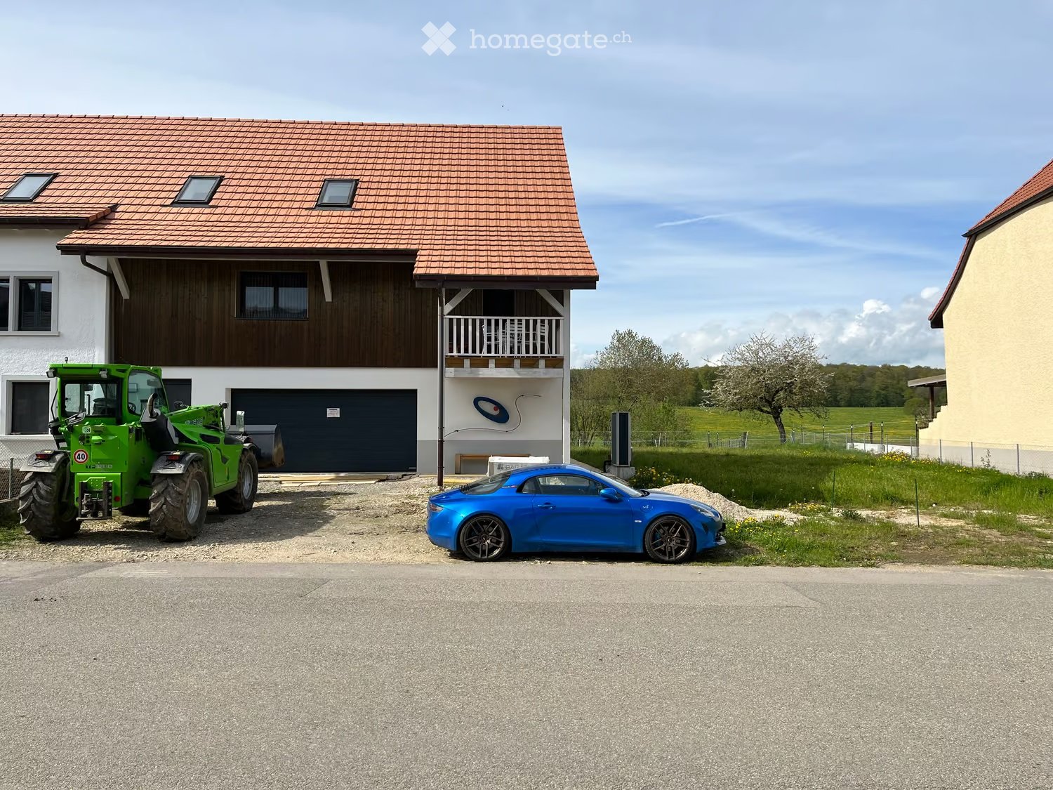 Two-story house with a red-tiled roof, white and brown exterior, garage, and balcony. A green tractor and a blue sports car are parked in front.