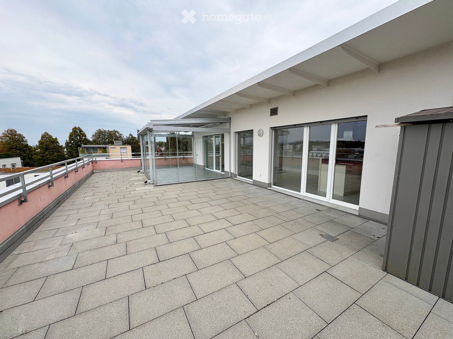 Modern rooftop terrace with tiled flooring, glass sliding doors, and a covered section with a pink accent wall.