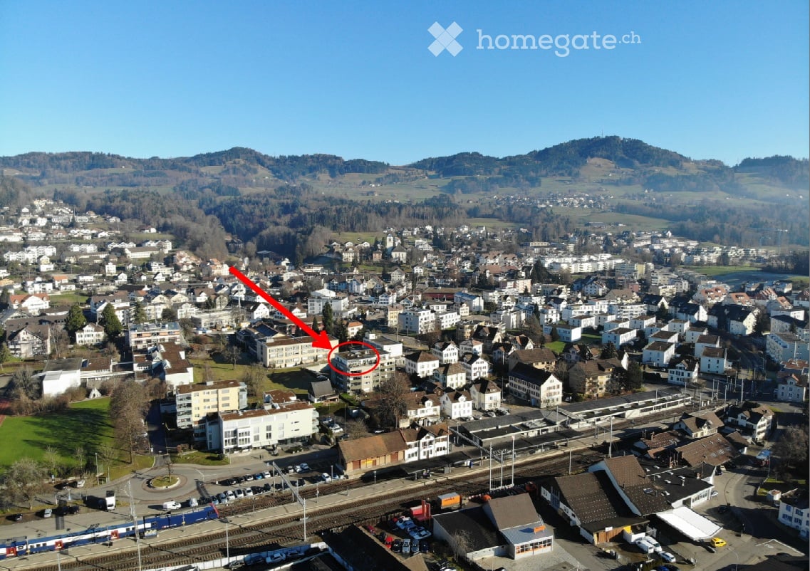 Aerial view of a town with numerous buildings, a train station, and surrounding hills.
