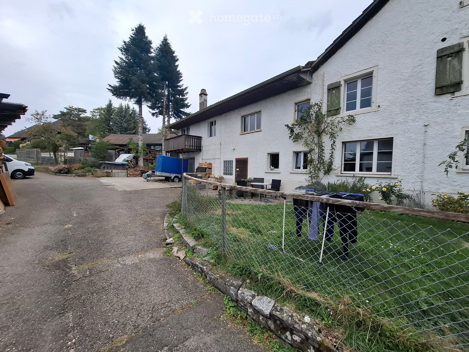Two-story white house with multiple windows, a balcony, and a fenced yard with a small table and chairs.