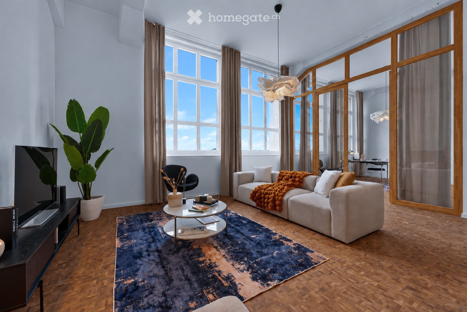 Modern living room with large windows, wooden flooring, a sofa with throw blankets, a coffee table, a TV, and a potted plant.