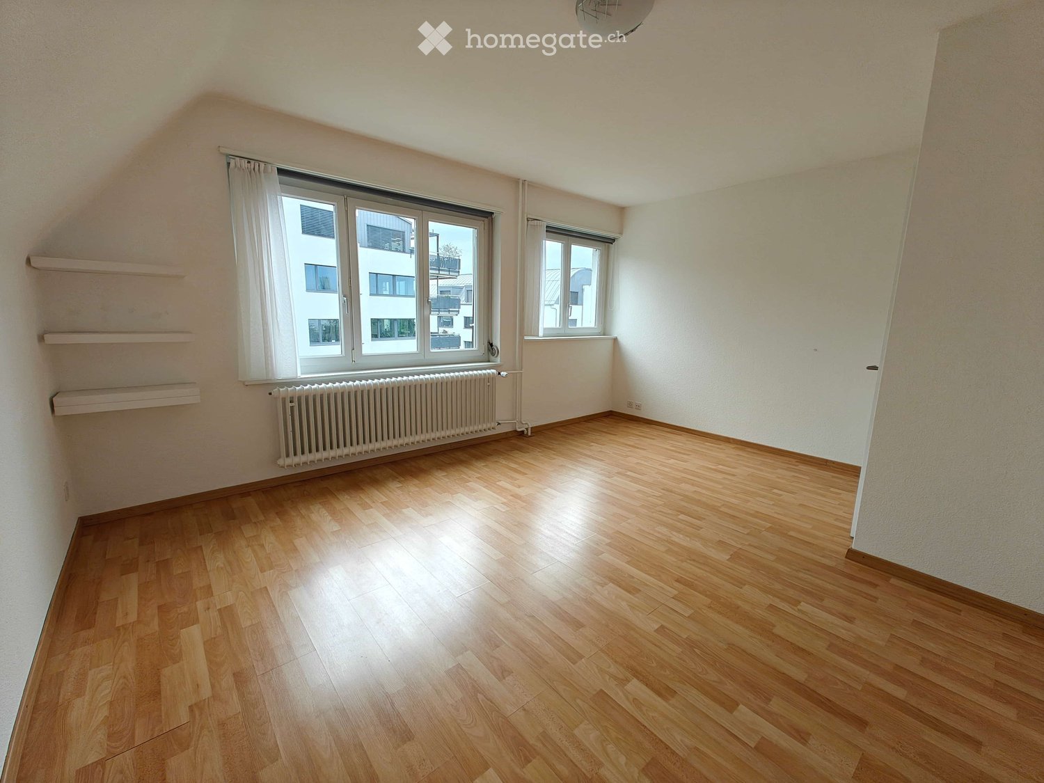 Empty room with wooden flooring, white walls, large windows with white curtains, radiator, and built-in shelves.