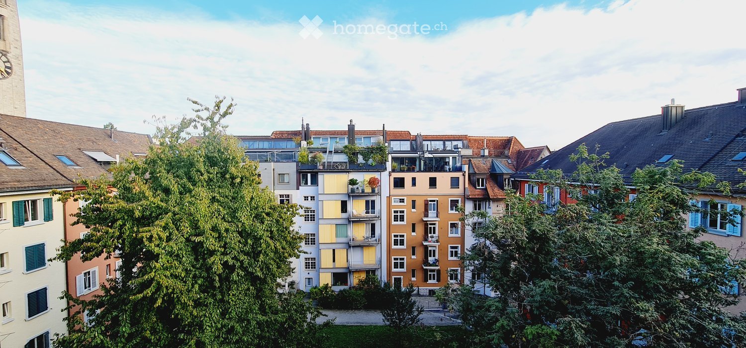 A row of multi-story residential buildings with varied facades, balconies, and greenery in front.