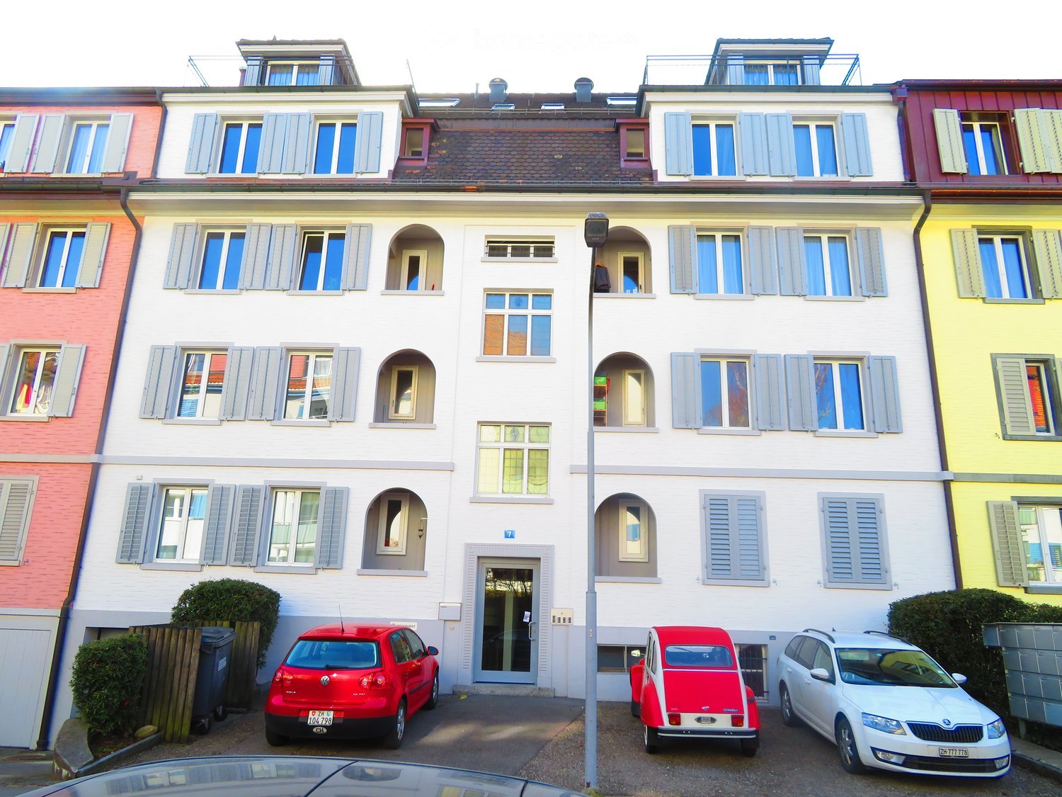 5 story building, white exterior, multiple windows, red car parked in front