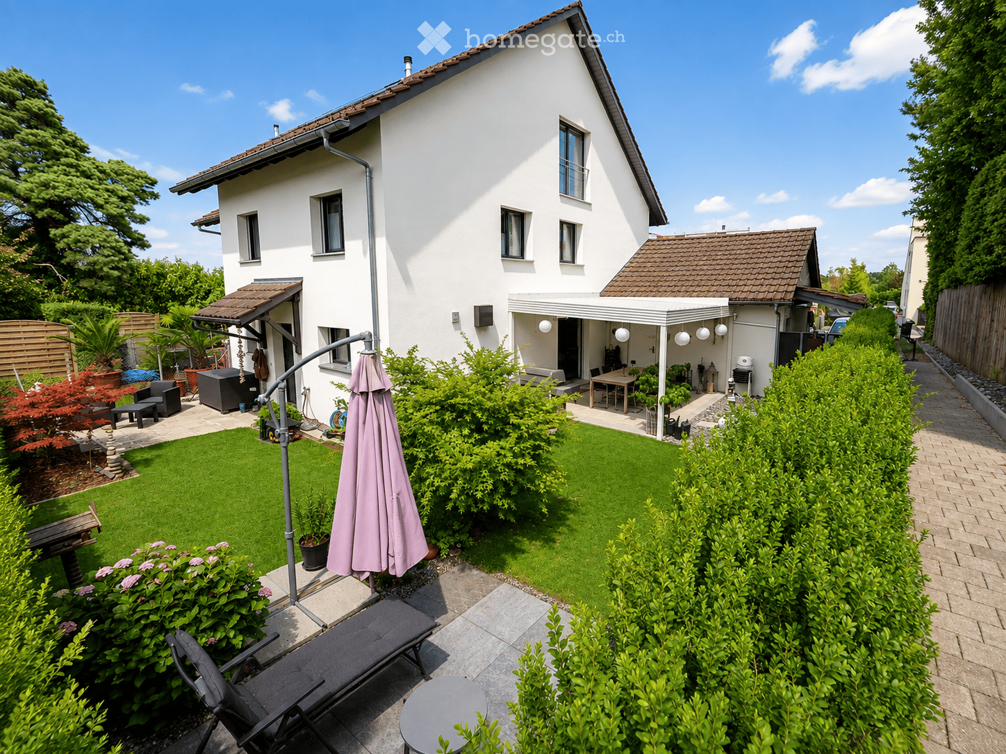 Well-maintained garden with a lawn, patio seating area, outdoor furniture, and a modern house in the background.