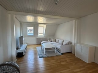 Bright living room with wooden flooring, white walls, large windows, grey sofa, white coffee table, TV stand, and cabinet.
