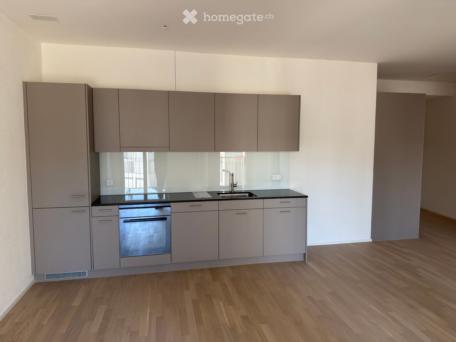 Modern kitchen with grey cabinets, a black countertop, a sink, and an oven. The floor is wooden.