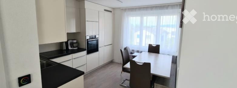 Modern kitchen and dining area with white cabinets, black countertop, built-in oven, coffee maker, and a dining table with four chairs.