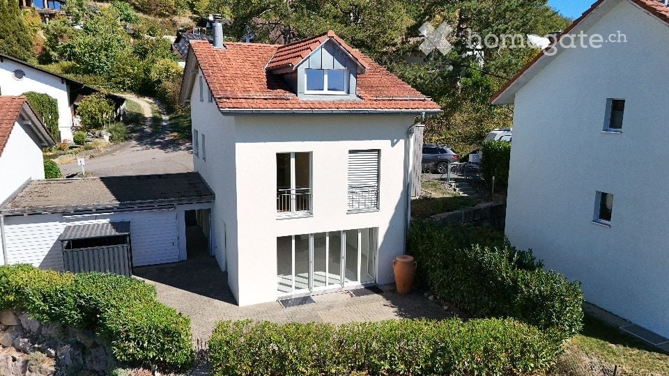 Two-story house with white exterior, red-tiled roof, garage, and parking area.