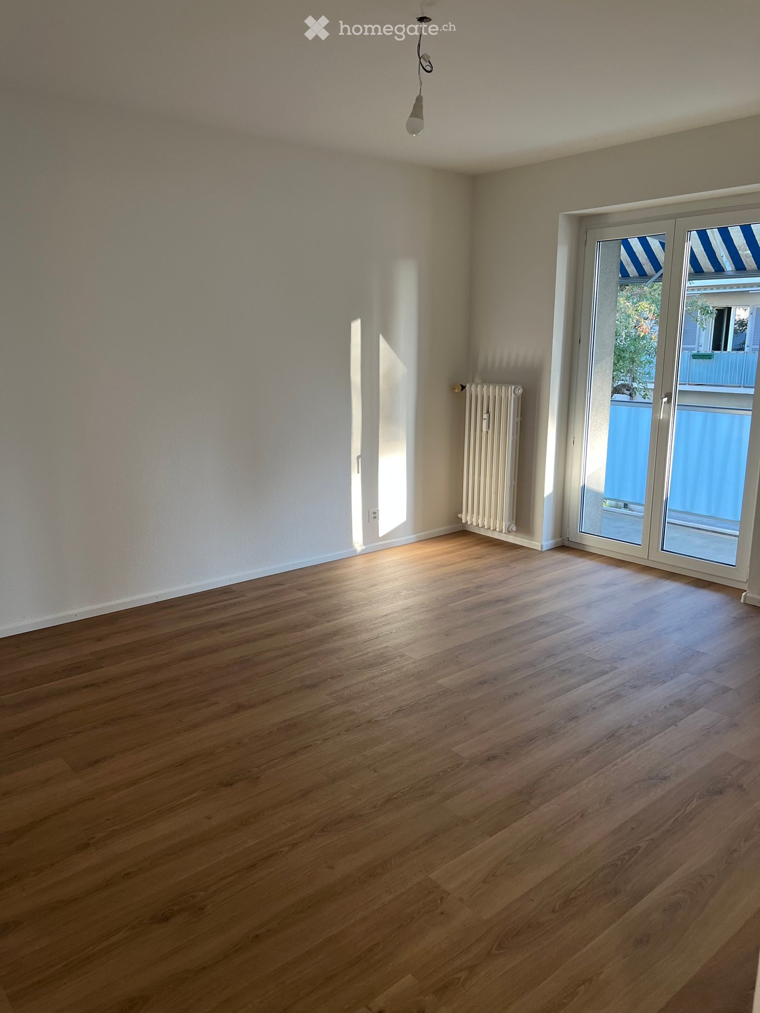 Empty room with wooden flooring, white walls, a radiator, and a large sliding glass door leading to a balcony.