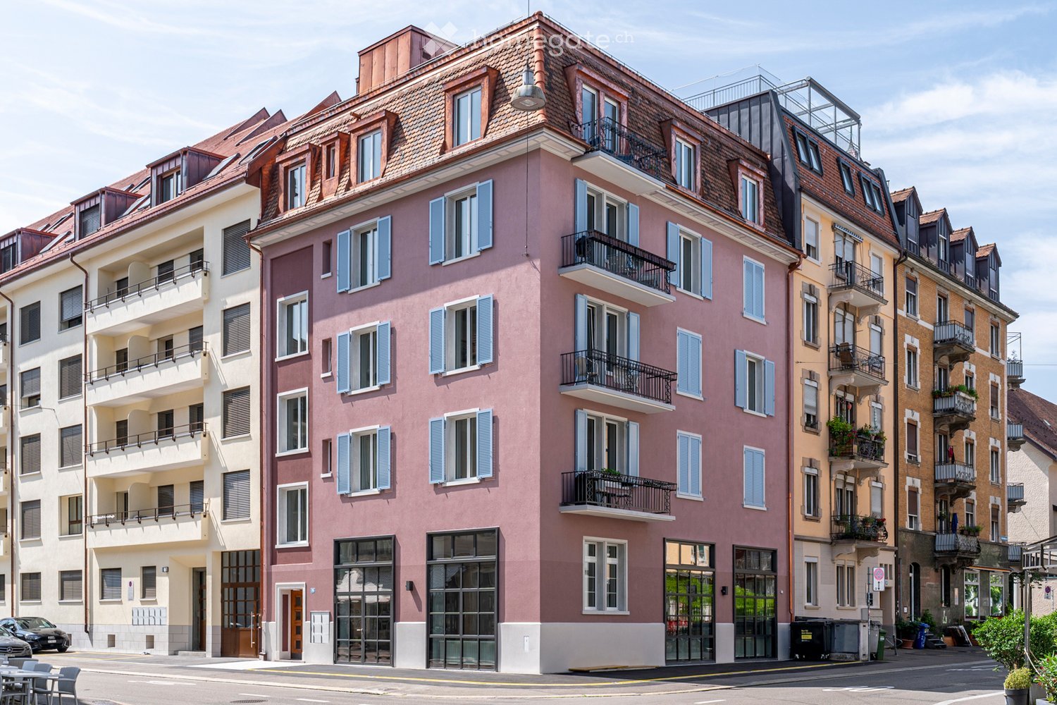 Multi-story residential building with pink facade, multiple balconies, and large windows. The building features a classic European architectural style with shutters and a tiled roof.