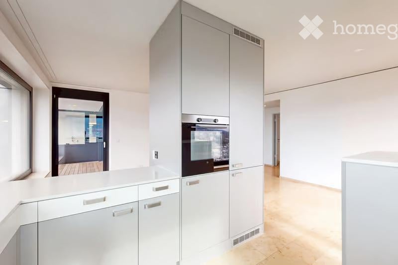 Modern kitchen with white cabinets, a built-in oven, and a light wooden floor.