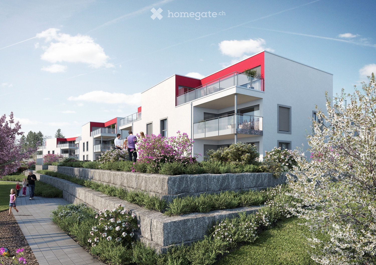 Modern residential building with white and red facade, multiple balconies, and surrounding garden area with flowering plants and trees.