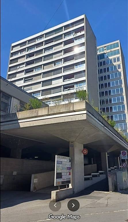 Modern multi-story apartment building with a covered parking area and signage.